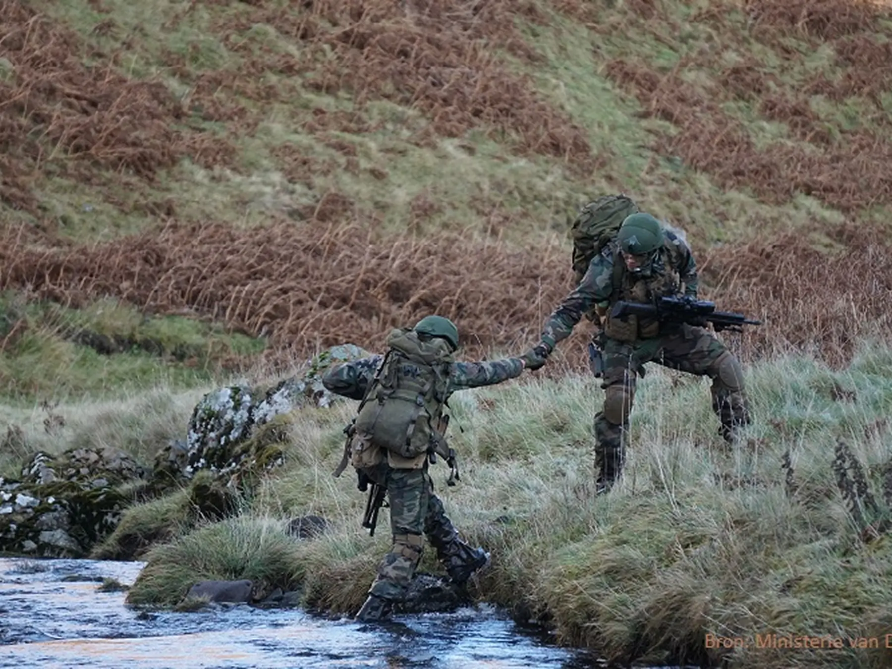 afbeelding van militairen die elkaar ondersteunen bij een rivier